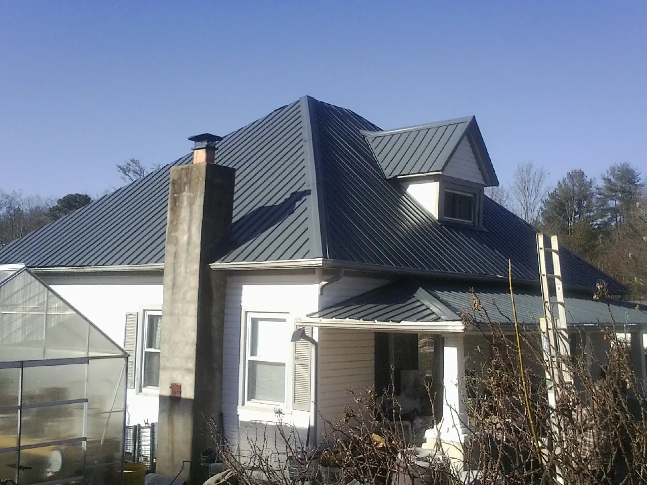 Dark blue standing seam metal roof on a white farmhouse with dormer — Slate & Tile Roof Repair by Roofing Brothers in Philipsburg
