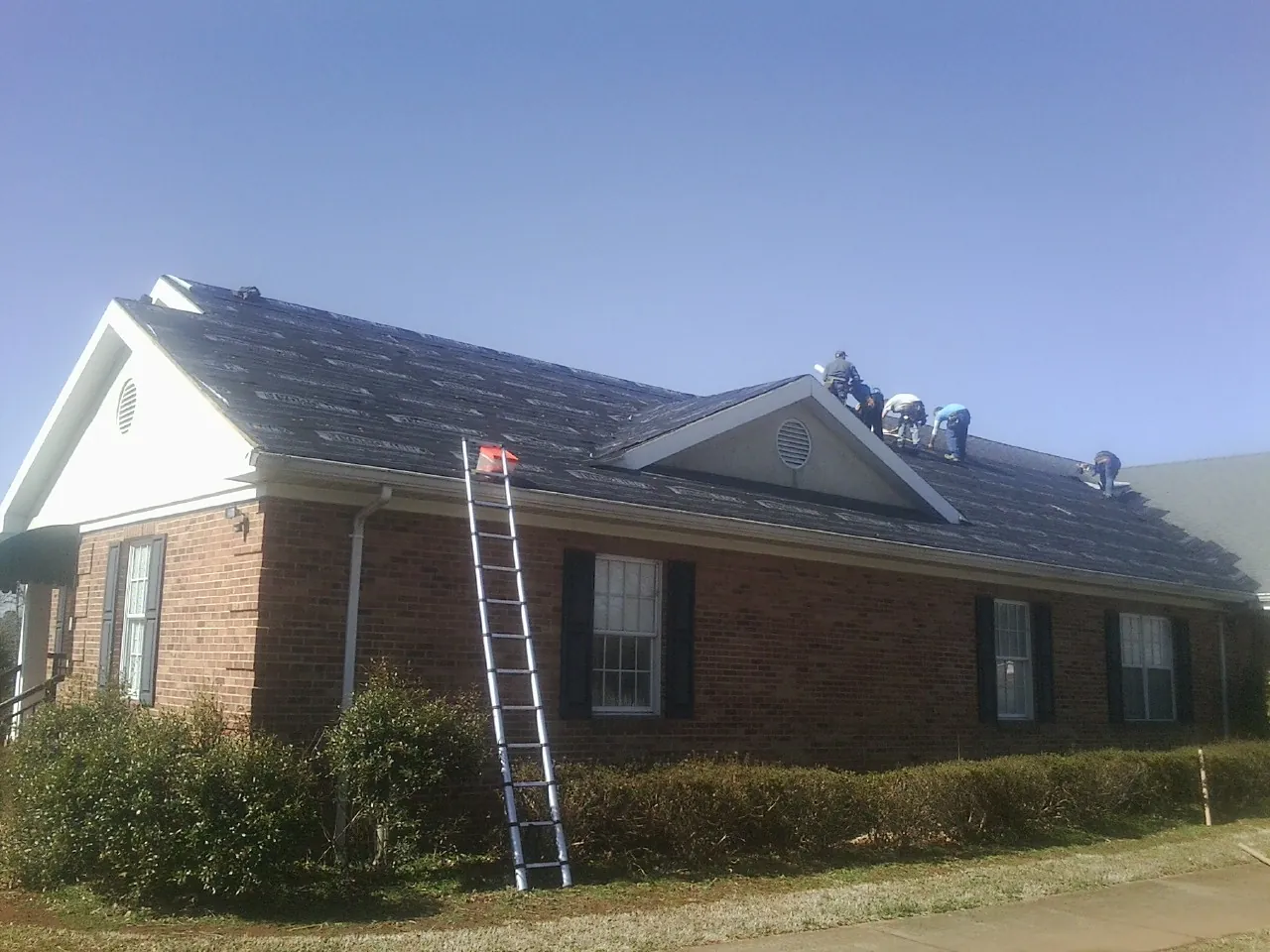 Crew tearing shingles off a brick ranch roof with a ladder set — Emergency Roof Repair work by our crew in Philipsburg
