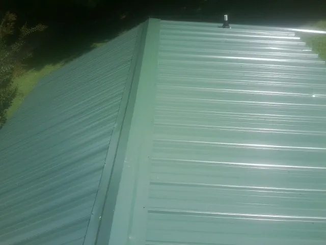 New green metal panels meeting at the ridge of a roof — Flat Roof Repair work by our crew in Philipsburg